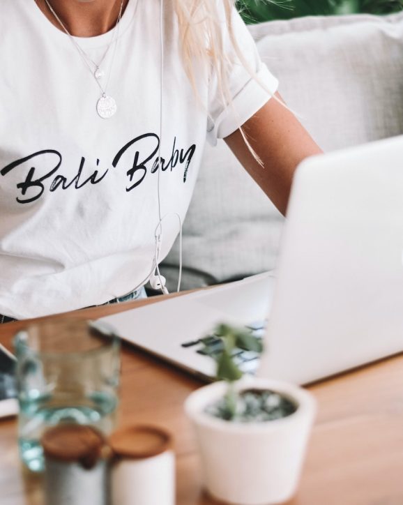 woman in white crew neck t-shirt sitting by the table with macbook