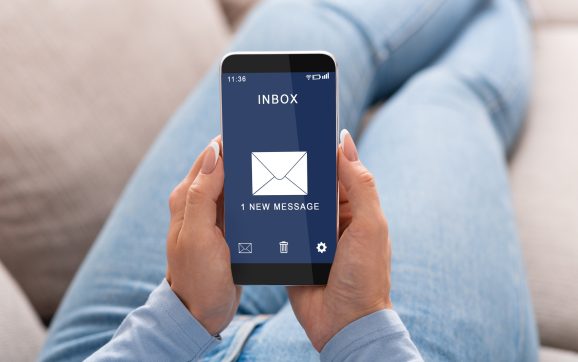 Woman Reading E-Mail Message On Smartphone Sitting On Couch Indoor