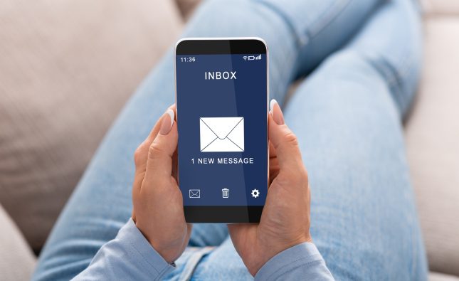 Woman Reading E-Mail Message On Smartphone Sitting On Couch Indoor